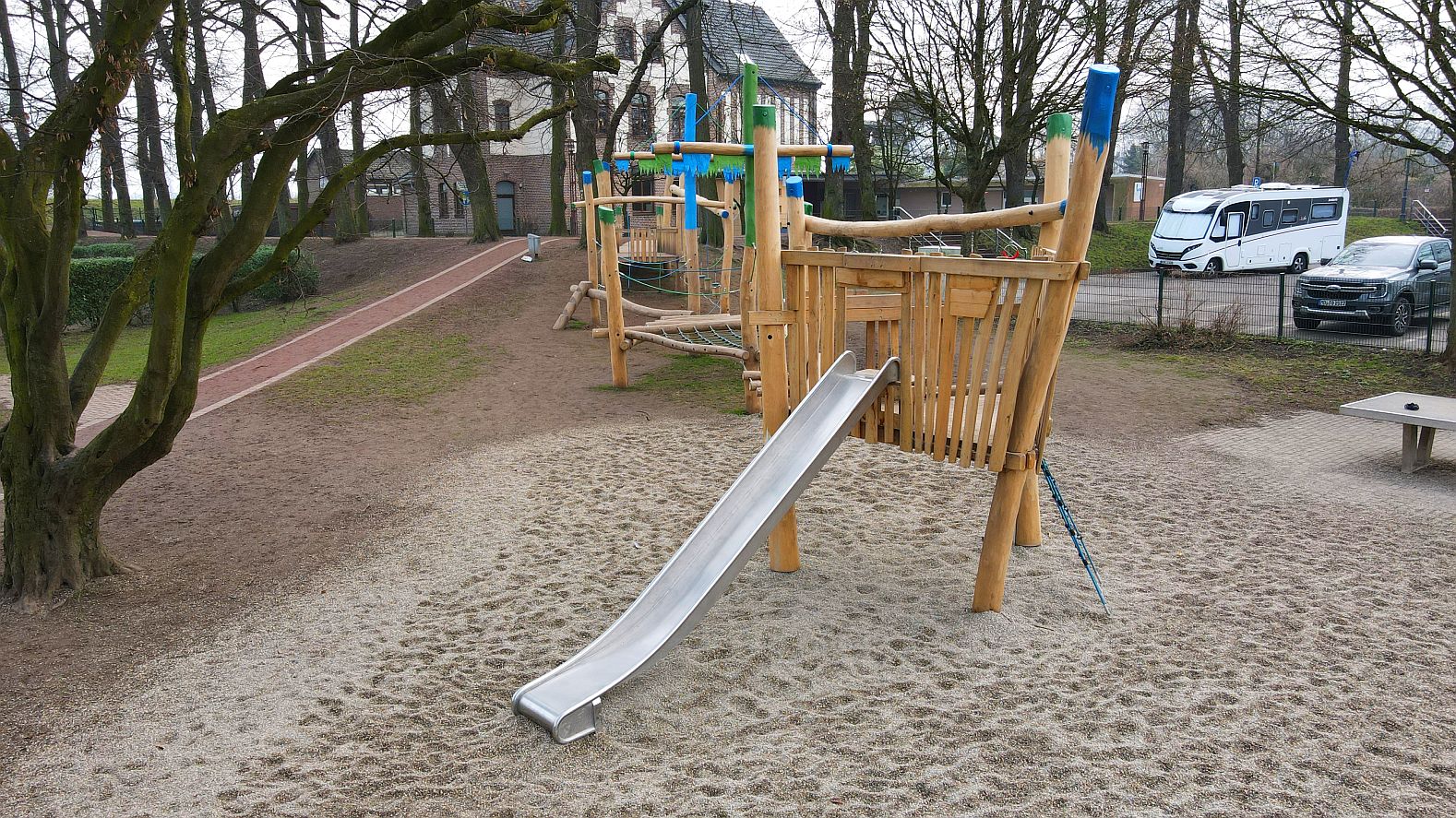 Langes Holz-Spielschiff mit Edelstahlrutsche, Kletterelementen und Hängebrücken – Spielplatz mit Naturmaterialien neben einer Schule