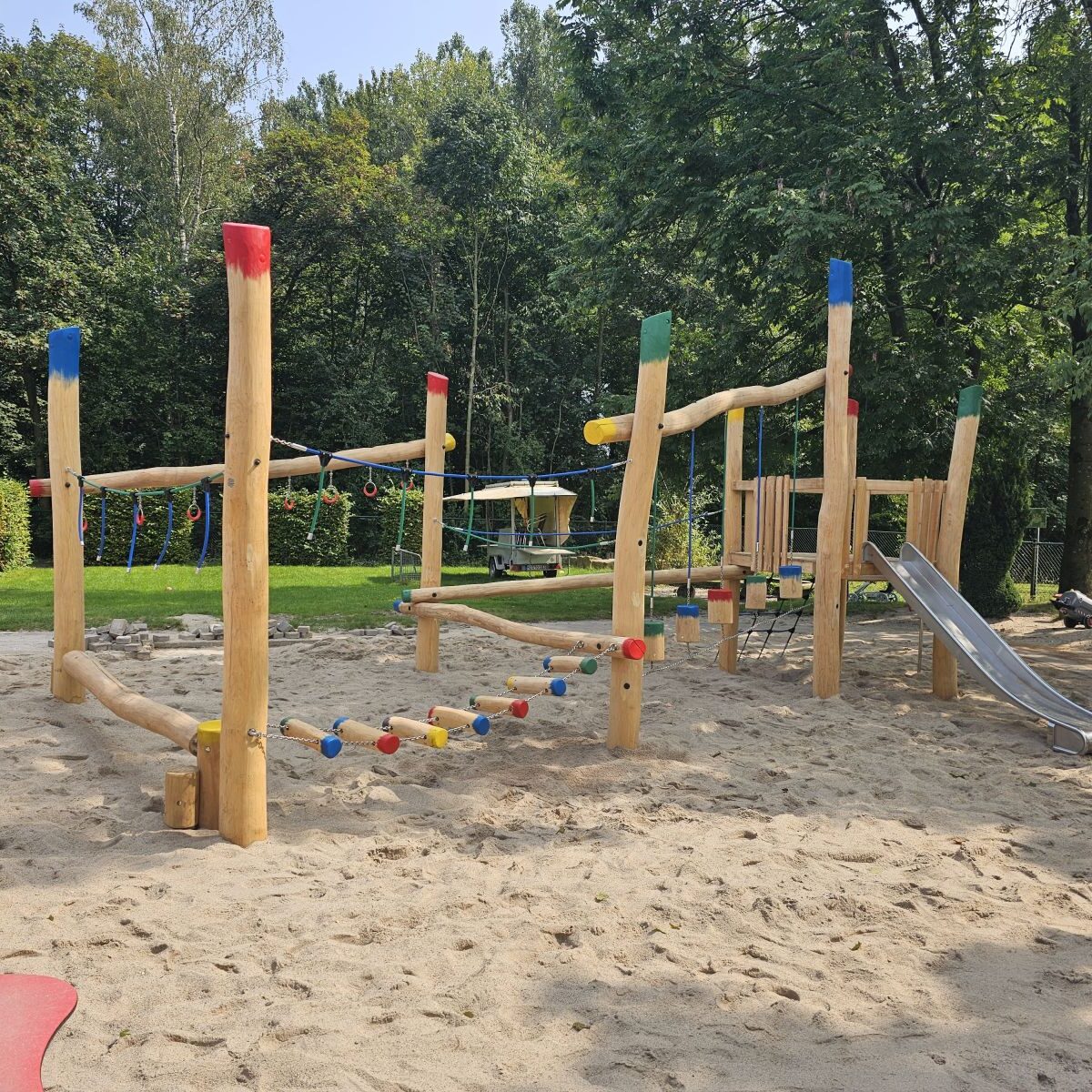 Kletterspielplatz-Kita-Kindergarten-Schule-naturnah Kinderseilgarten aus Robinienholz mit Kletterelementen und Rutsche auf Sandfläche, umgeben von Bäumen