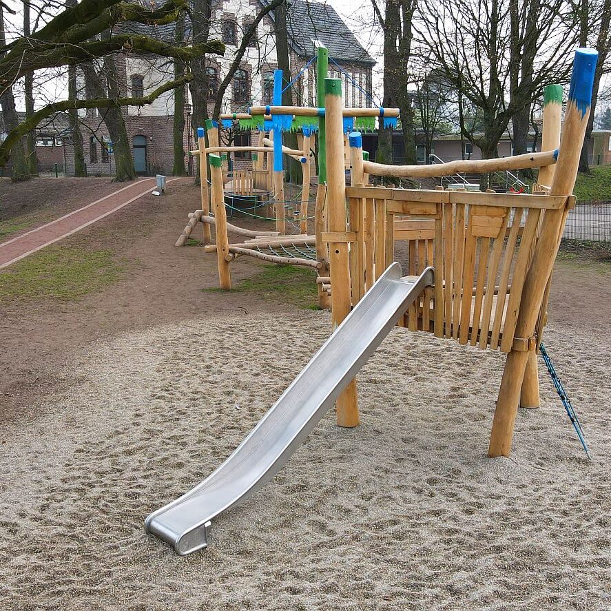 holz-spielschiff-rutsche-kletterelemente-schulspielplatz-robinie Langes Holz-Spielschiff mit Edelstahlrutsche, Kletterelementen und Hängebrücken – Spielplatz mit Naturmaterialien neben einer Schule