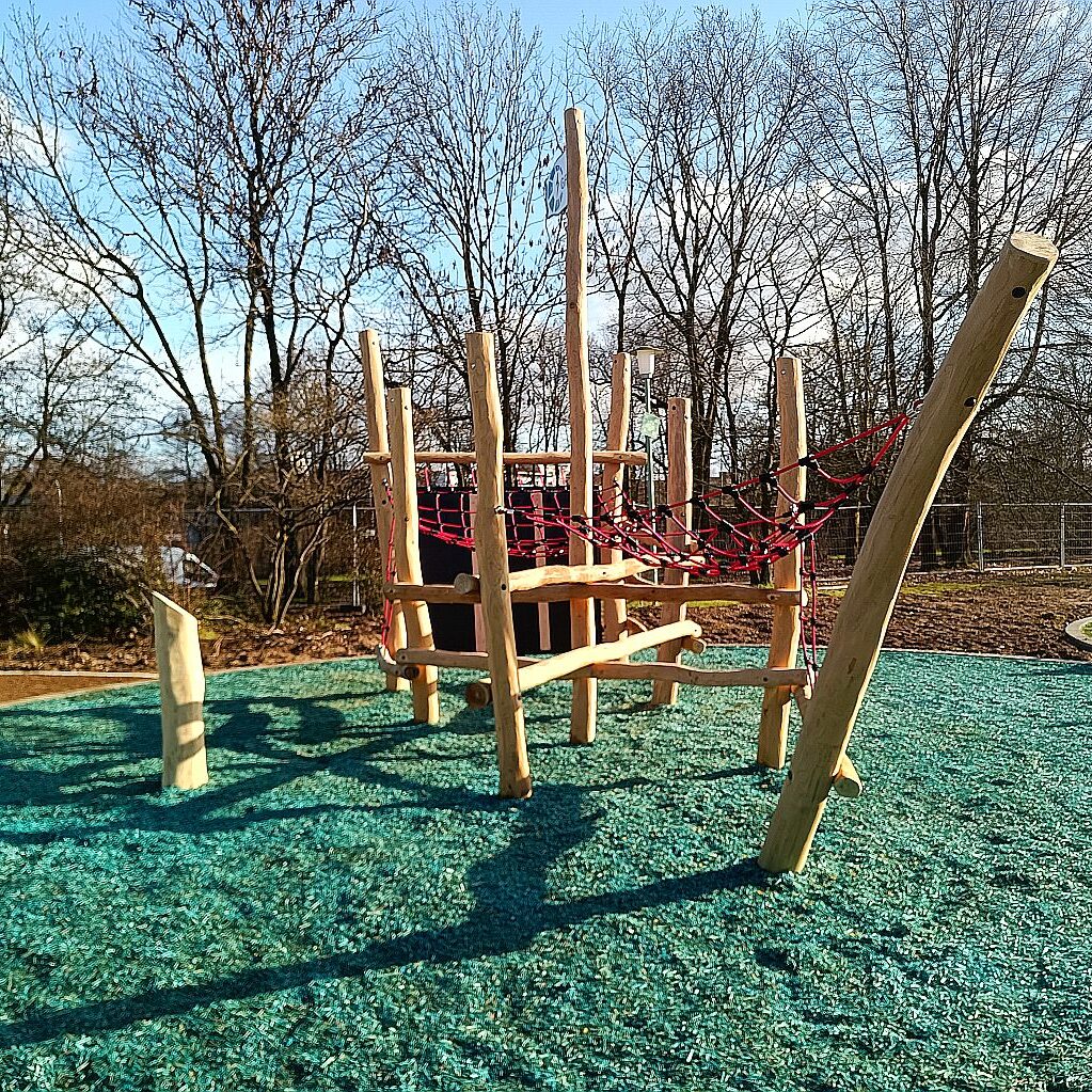 spielschiff-netzbruecken-klettern-chillen Holz-Spielschiff mit roten Netzbrücken und Kletterelementen auf weichem, blaugrünem Fallschutzboden – ideal zum Klettern und Entspannen